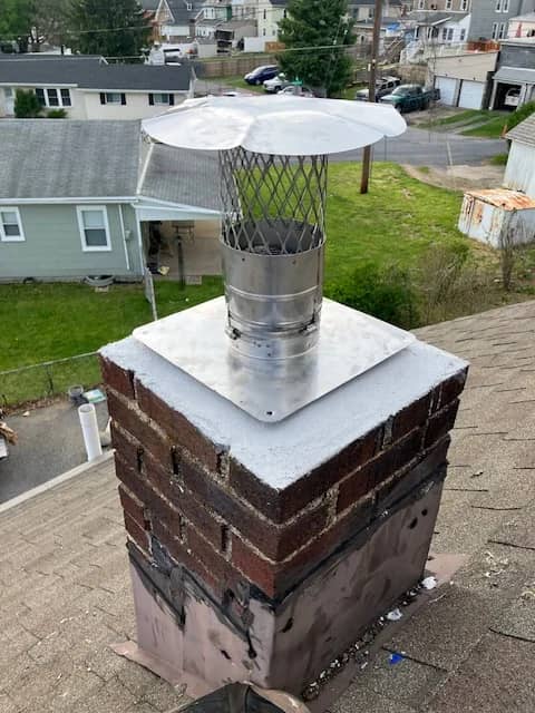 Light-colored chimney crown beneath a stainless steel liner cap.
