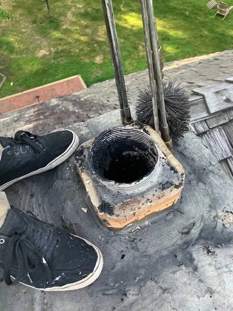 Chimney sweeping brush beside a flue opening on a roof.